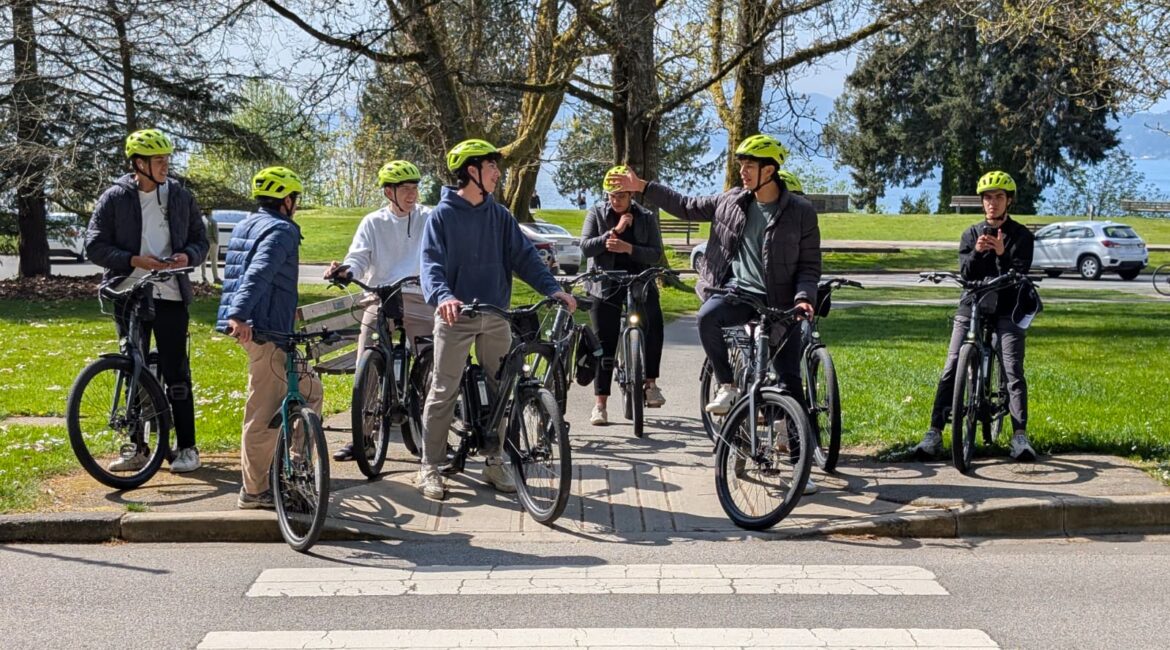 Group of tourists riding electric rental bikes from YesCycle on a sunny day near Stanley Park seawall.