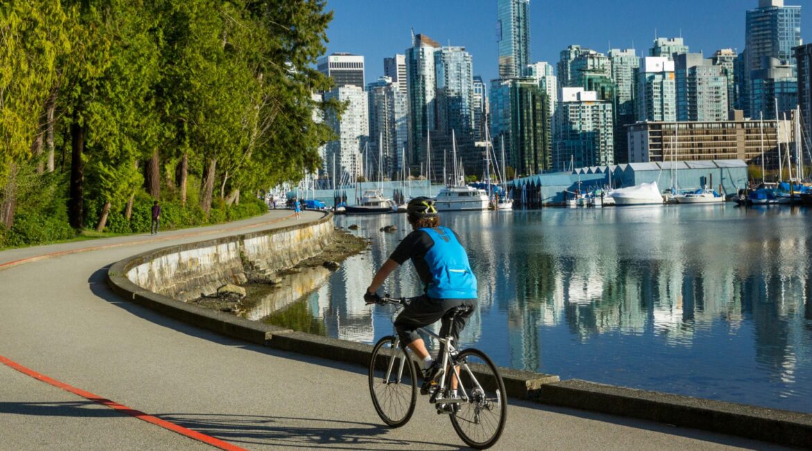 Cyclist riding the Stanley Park Seawall with the downtown Vancouver skyline across Coal Harbour