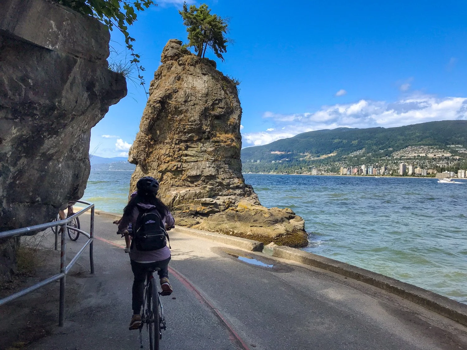 Cyclist riding past Siwash Rock on the Stanley Park Seawall